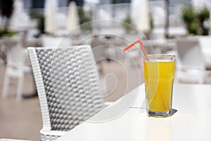 Glass of orange juice with plastic straw on white table in restaurant outdoor lounge zone