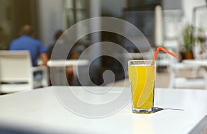 Glass of orange juice with plastic straw on white table in restaurant outdoor lounge zone
