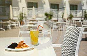 Glass of orange juice with plastic straw on white table in restaurant outdoor lounge zone