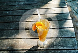 a glass of orange juice on the sandy beach. Fresh orange juice, fruits on sand with wooden background, summer concept