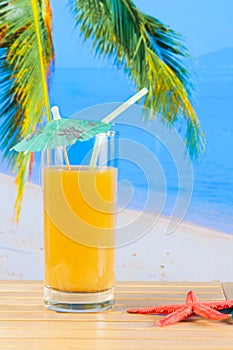 Glass of orange juice on the sandy beach near starfish