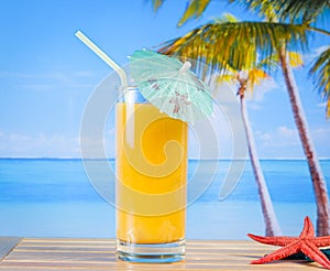 Glass of orange juice on the sandy beach near starfish