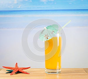 Glass of orange juice on the sea and sandy beach near starfish