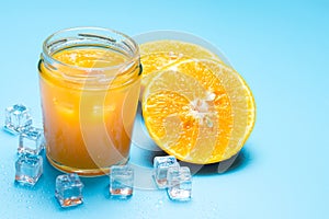 Glass of orange juice with sliced orange fruit and ice cubes on blue