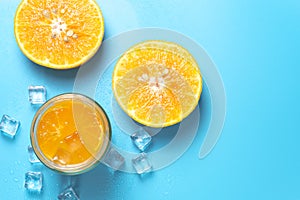 Glass of orange juice with sliced orange fruits with ice cubes on blue background