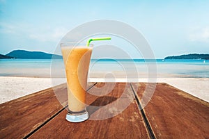 A glass of orange juice stands on a wooden table. Cocktail on the background of the blue sea. Vacation, vacation, summer, pleasure