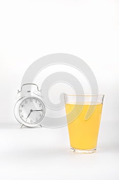 Glass of orange juice on a white background. Behind is a white alarm clock. Healthy food concept. Space for text