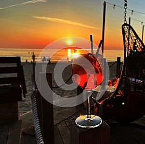 Glass of orange limonade on wooden top at sea beach on pink sunset leisure holiday relaxing lifestyle