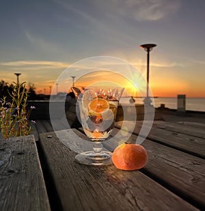 Glass of orange water and mandarine  freshness  on wooden table  and flowers on promenade at sunset in sea people relax summer photo