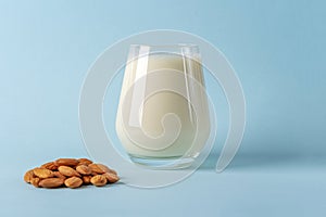 Glass of organic vegan dairy free milk from almonds nuts. Healthy breakfast with vegetarian alternative drink on blue background.