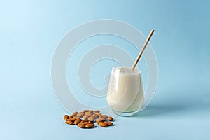 Glass of organic vegan dairy free milk from almonds nuts. Healthy breakfast with vegetarian alternative drink on blue background.