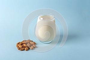 Glass of organic vegan dairy free milk from almonds nuts. Healthy breakfast with vegetarian alternative drink on blue background.