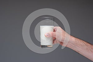 Glass of pasteurised milk hand by Caucasian male hand. Close up studio shot,  on gray photo