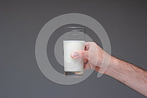 Glass of pasteurised milk hand by Caucasian male hand. Close up studio shot,  on gray