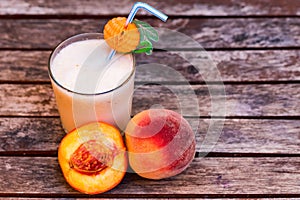 Glass of peach yoghurt and peaches on wooden table