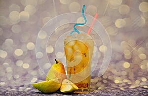 A glass of pear juice with ice and straws stands on a gray shiny background next to ripe fruits