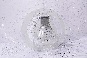 Glass perfume bottle with silver sequins on light background