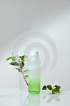 A glass petri dish and beaker containing plant branches arranged with a bottle with empty label over white background