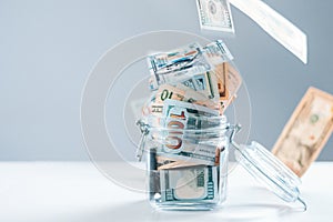 Glass piggy bank full of money. Banknotes are strewed from above. The concept of squandering
