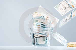 Glass piggy bank full of money. Banknotes are strewed from above. The concept of squandering