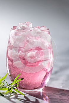 The glass of pink drink with ice and rosemary