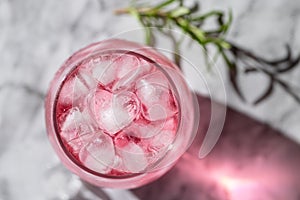 The glass of pink drink with ice and rosemary on background