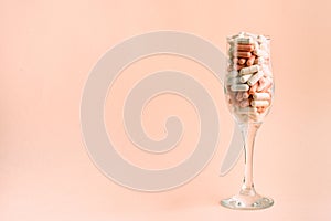 Glass with pink and white capsules. Medicines instead of a party. Copy space