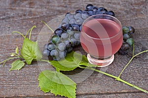 a glass of pink wine and a bunch of grapes and grape leaves