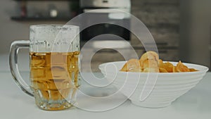 A glass pint mug of pilsener or lager beer with potato chips are in the kitchen