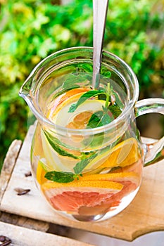 Glass pitcher with detox infused citrus water with grapefruits, oranges, limes, lemons, fresh mint, wooden garden fruit box, green