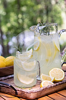 Glass and pitcher of lemonade with lemons and rosemary