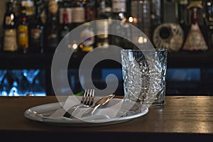 Glass, plate, fork and knife in a restaurante, bar in background. photo