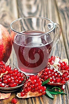 Glass of pomegranate juice with ripe fresh punica granatum fruits with leaves on wooden table