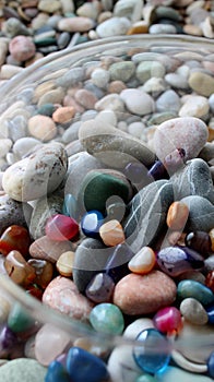Glass pot with colorful quartz gem stones over a tray with gray sea pebbles