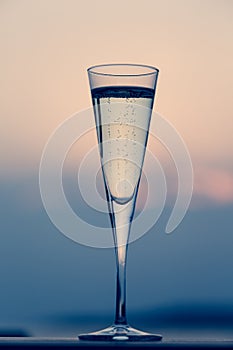 Glass of prosecco at a wooden pier at sunset. Luxury resort vacation concept. Festive relax getaway background.