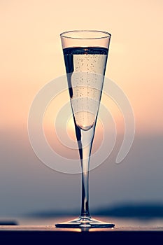 Glass of prosecco at a wooden pier at sunset. Luxury resort vacation concept. Festive relax getaway background.