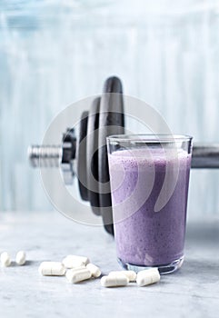 Glass of Protein Shake with milk and blueberries, Beta-alanine capsules and a dumbbell in background. Sports bodybuilding nutritio