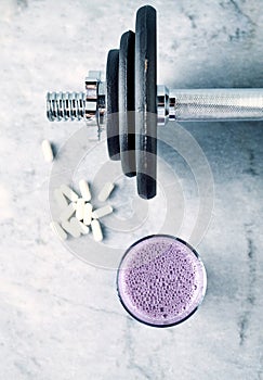 Glass of Protein Shake with milk and blueberries, Beta-alanine capsules and a dumbbell in background. Sports bodybuilding nutritio