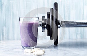 Glass of Protein Shake with milk and blueberries, Beta-alanine capsules and a dumbbell in background. Sports bodybuilding nutritio