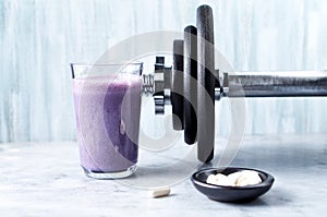 Glass of Protein Shake with milk and blueberries, Beta-alanine capsules and a dumbbell in background. Sports bodybuilding nutritio