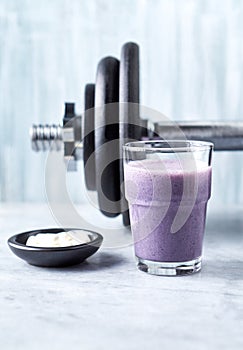 Glass of Protein Shake with milk and blueberries, Beta-alanine capsules and a dumbbell in background. Sports bodybuilding nutritio