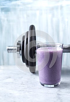 Glass of Protein Shake with milk and blueberries and a dumbbell in background. Sports bodybuilding nutrition