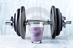 Glass of Protein Shake with milk and blueberries and a dumbbell in background. Sports bodybuilding nutrition.