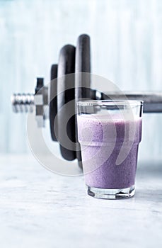 Glass of Protein Shake with milk and blueberries and a dumbbell in background. Sports bodybuilding nutrition.