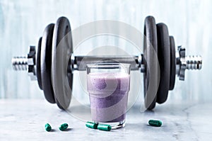 Glass of Protein Shake with milk and blueberries, L-Carnitine capsules and a dumbbell in background. Sports bodybuilding nutrition