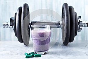Glass of Protein Shake with milk and blueberries, L-Carnitine capsules and a dumbbell in background. Sports bodybuilding nutrition