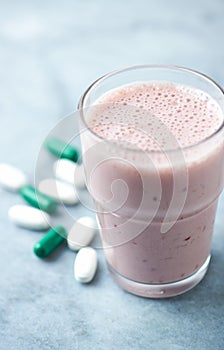 Glass of Protein Shake with milk and raspberries. BCAA amino acids and L - Carnitine capsules in background. Sport nutrition.