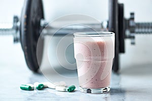 Glass of Protein Shake with milk and raspberries. BCAA amino acids, L - Carnitine capsules and a dumbbell in background. Sport nut