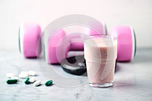 Glass of Protein Shake with milk and raspberries. BCAA amino acids, L - Carnitine capsules and pink dumbbells in background. Sport