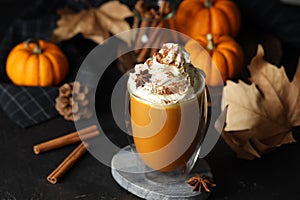 Glass of pumpkin spice latte with whipped cream and ingredients on black table